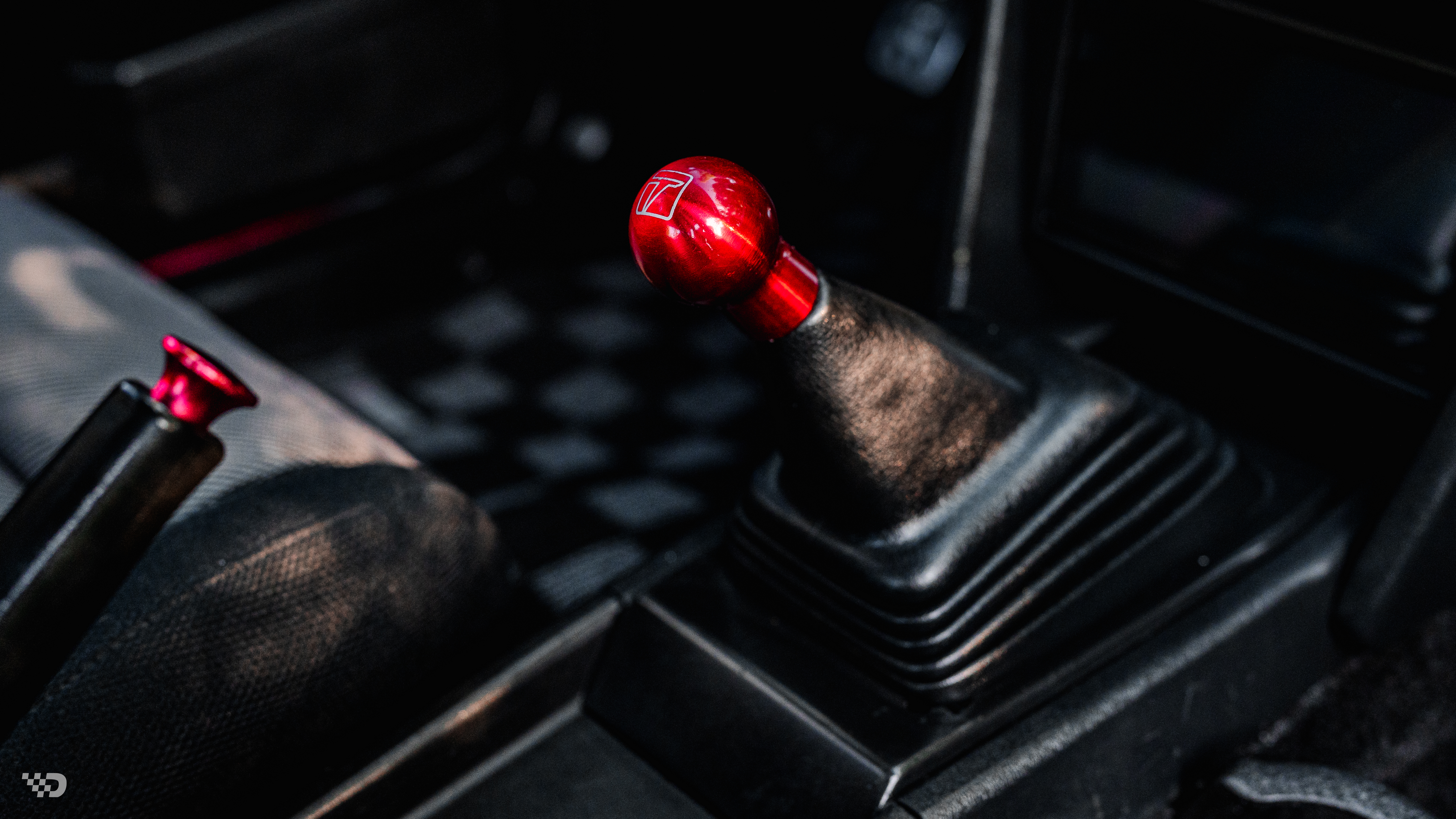 Close-up of red shift knob on manual shifter in AE86 interior.