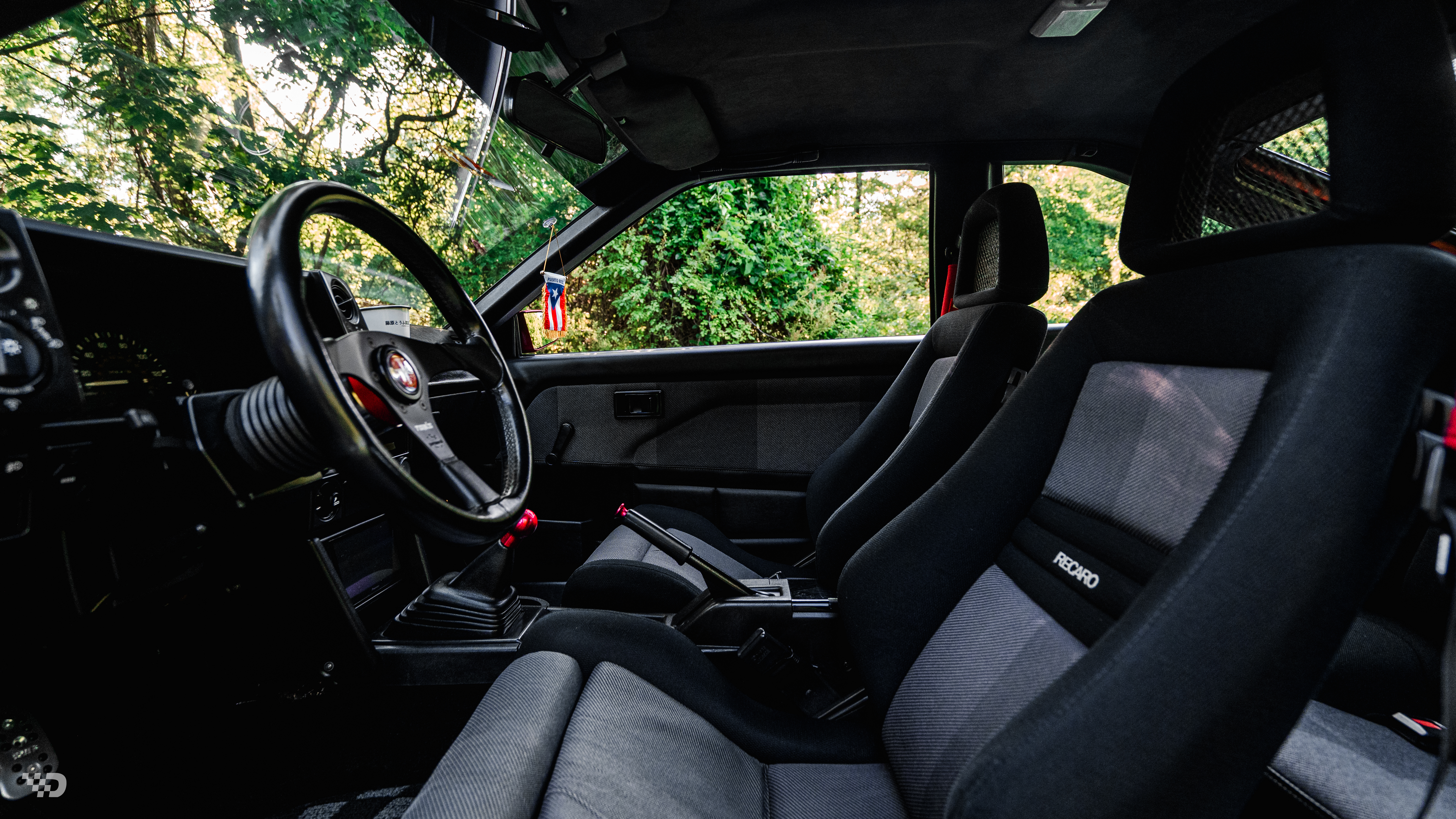 AE86 interior with Recaro seats, TOM’S steering wheel, and clean black cabin layout.
