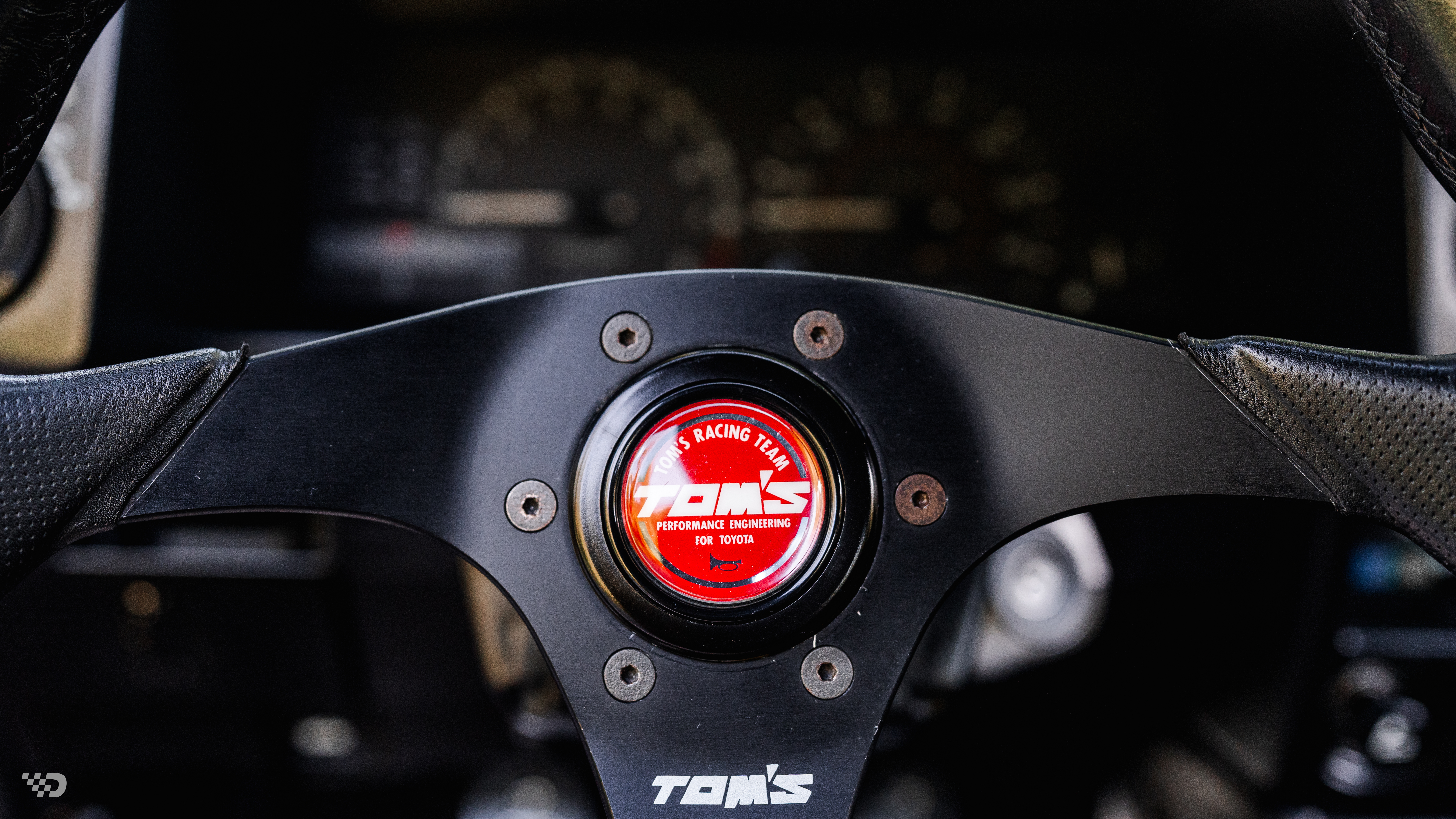 Close-up of TOM’S steering wheel center with red horn button.