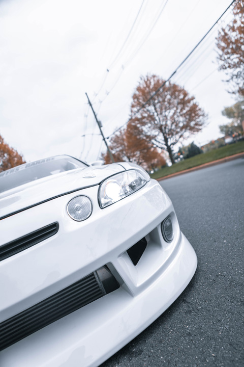 Close-up detail of the front end and BN Sports bumper on Aum Sung’s white 1992 Lexus SC400.
