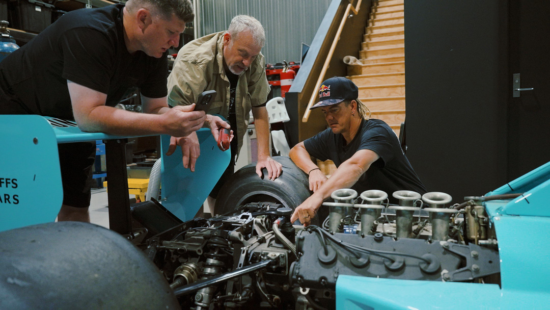 Team members inspecting the teal March Formula One chassis during the FORMIDABUL drift car build.