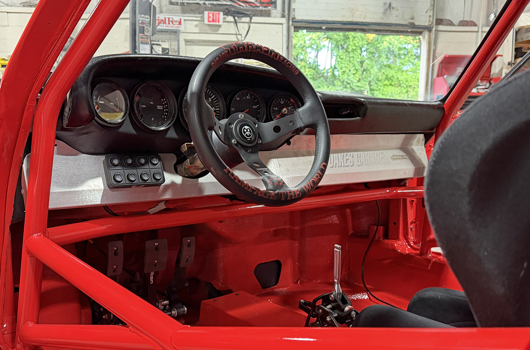 Interior of Jimmy Oakes’ Porsche 911 SC Porrari showing the roll cage, race steering wheel, custom dash, pedals, and shifter.