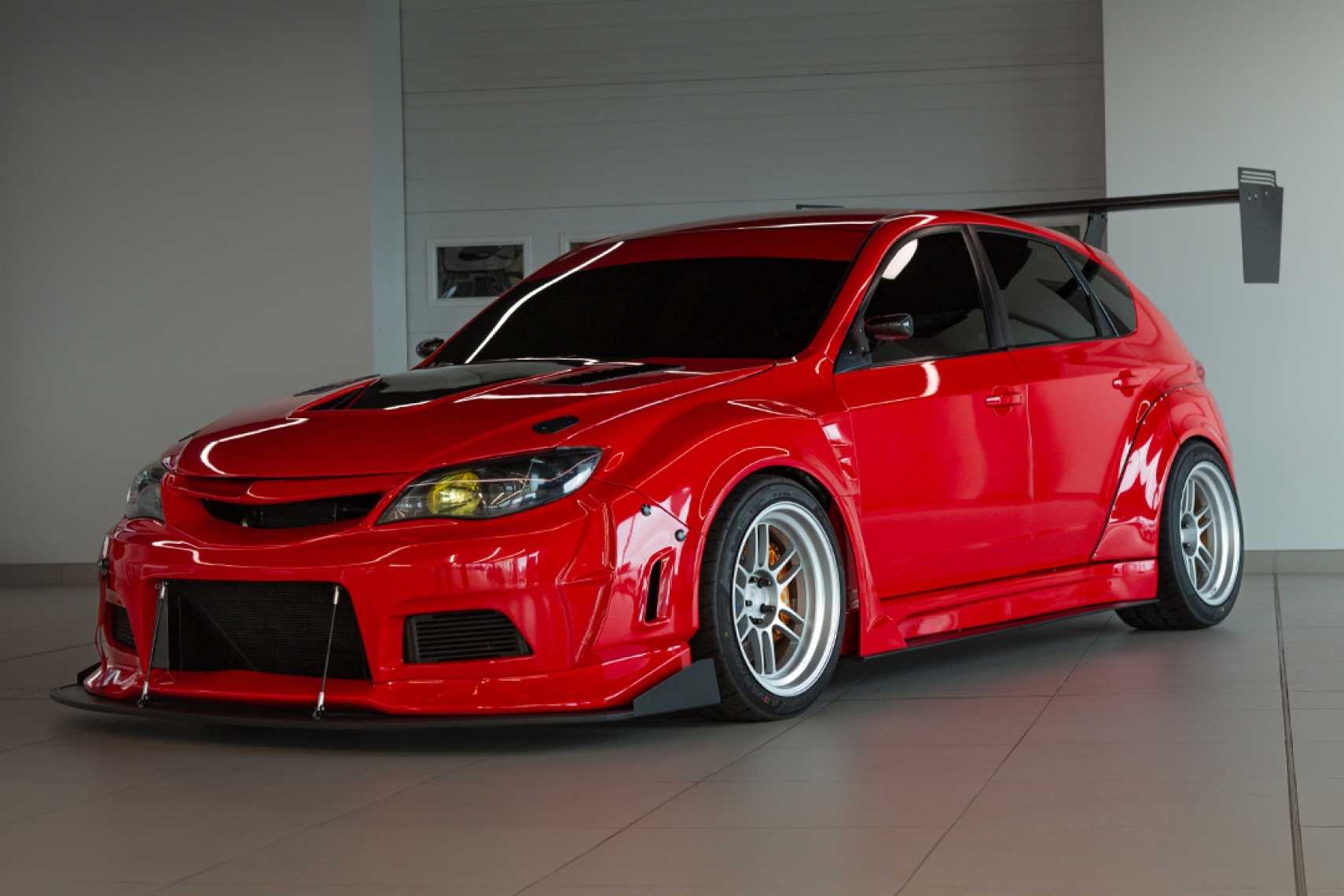 Jon Erickson’s red LS-swapped 2011 Subaru STi with widebody aero, front splitter, white wheels, and large rear wing.