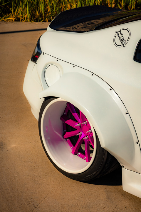 Rear quarter detail of Jordyn Brazeau’s white widebody 2006 Infiniti G35 showing the widened fender, pink Weds Kranze Vishnu wheel, and carbon duckbill trunk.