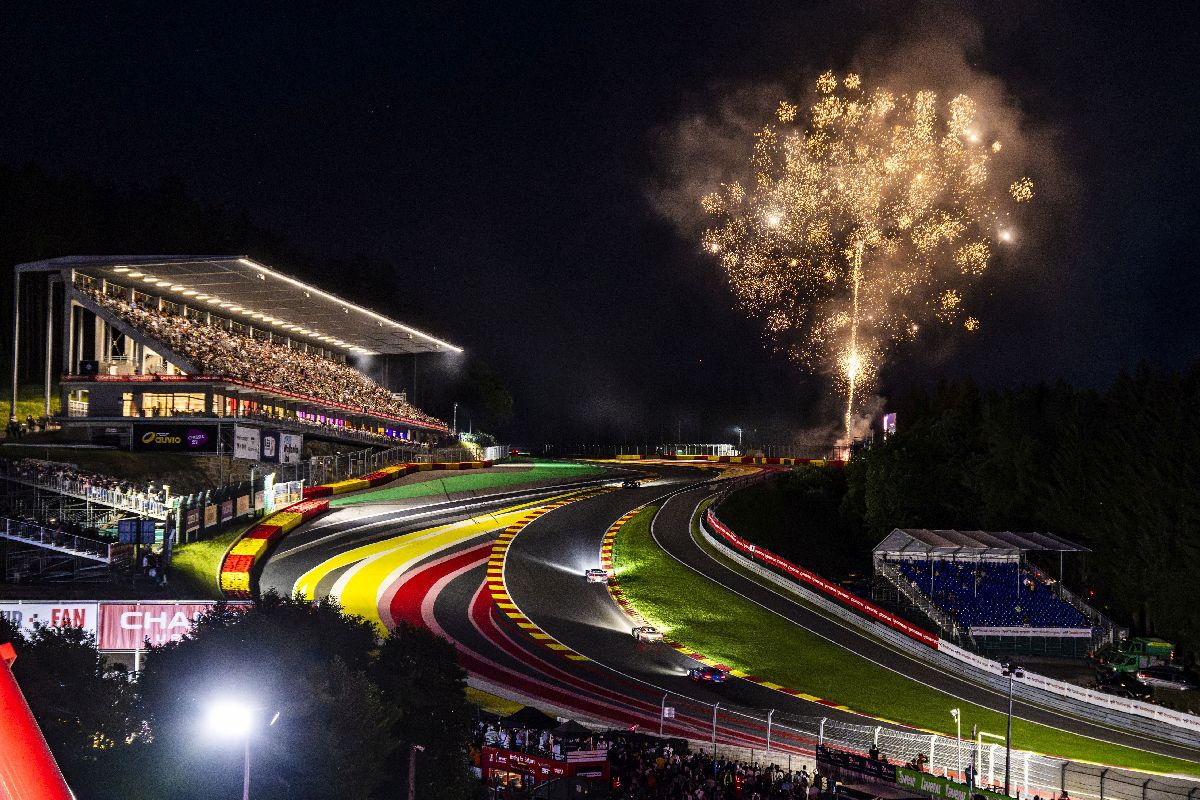 GT3 race cars climbing through Circuit de Spa-Francorchamps at night with fireworks above the grandstands.