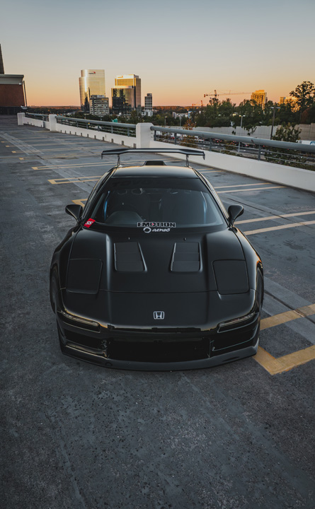 Front view of Peter Doan’s black 1991 Honda NSX parked on a rooftop garage with city skyline in the background.