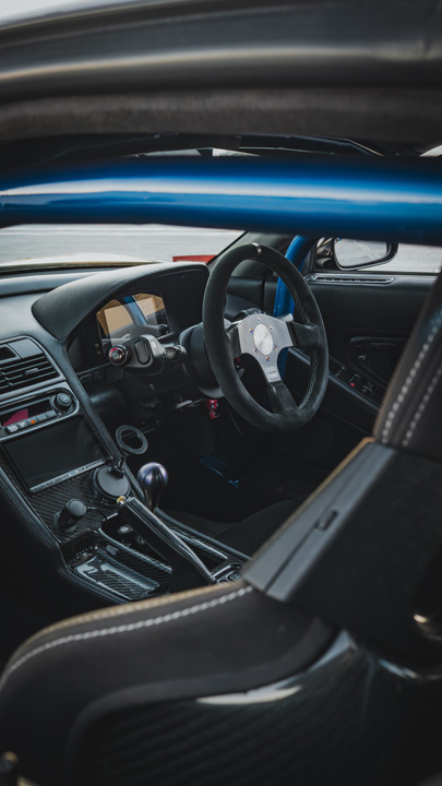 Interior detail of Peter Doan’s 1991 Honda NSX showing the right-hand-drive cockpit, blue Cusco roll cage, carbon trim, and aftermarket steering wheel.
