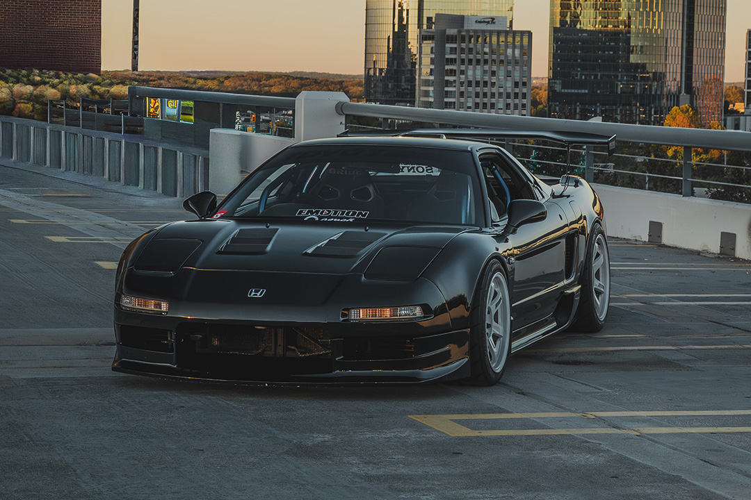 Front three-quarter view of Peter Doan’s black 1991 Honda NSX parked on a rooftop garage with white Volk Racing TE37 wheels and city skyline in the background.