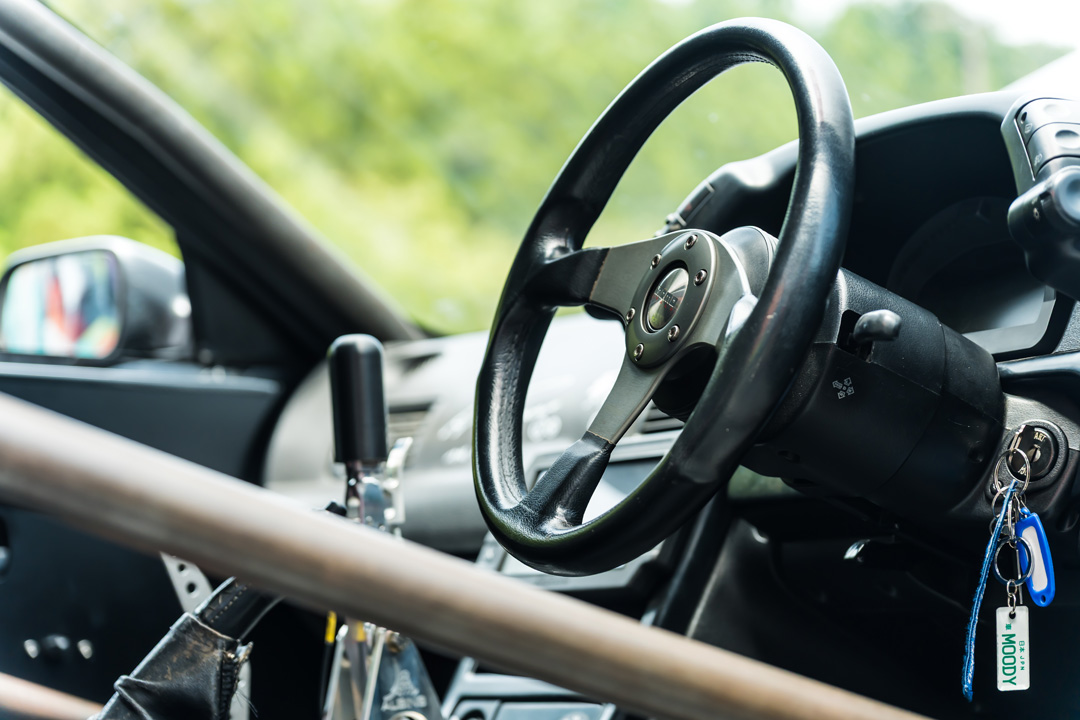 Interior detail of Cee Vann’s 1990 Nissan Skyline GT-R showing the Momo steering wheel, roll cage, sequential shifter, and right-hand-drive cockpit.
