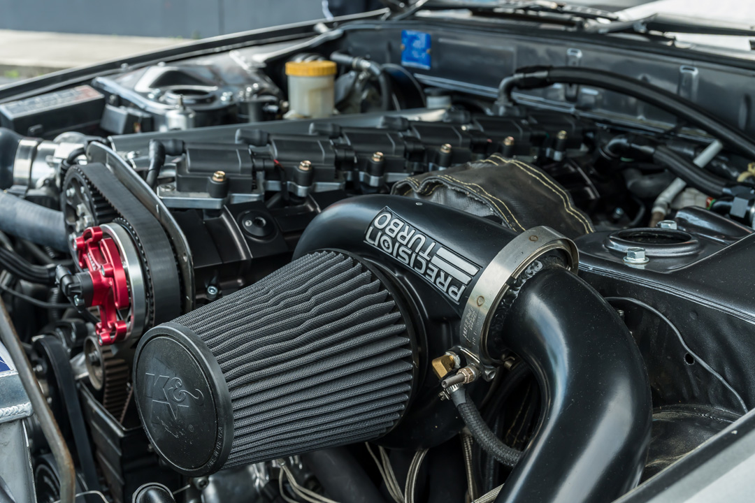 Close-up of Cee Vann’s 1990 Nissan Skyline GT-R showing the Precision turbo intake, K&N filter, timing hardware, and RB engine bay details.