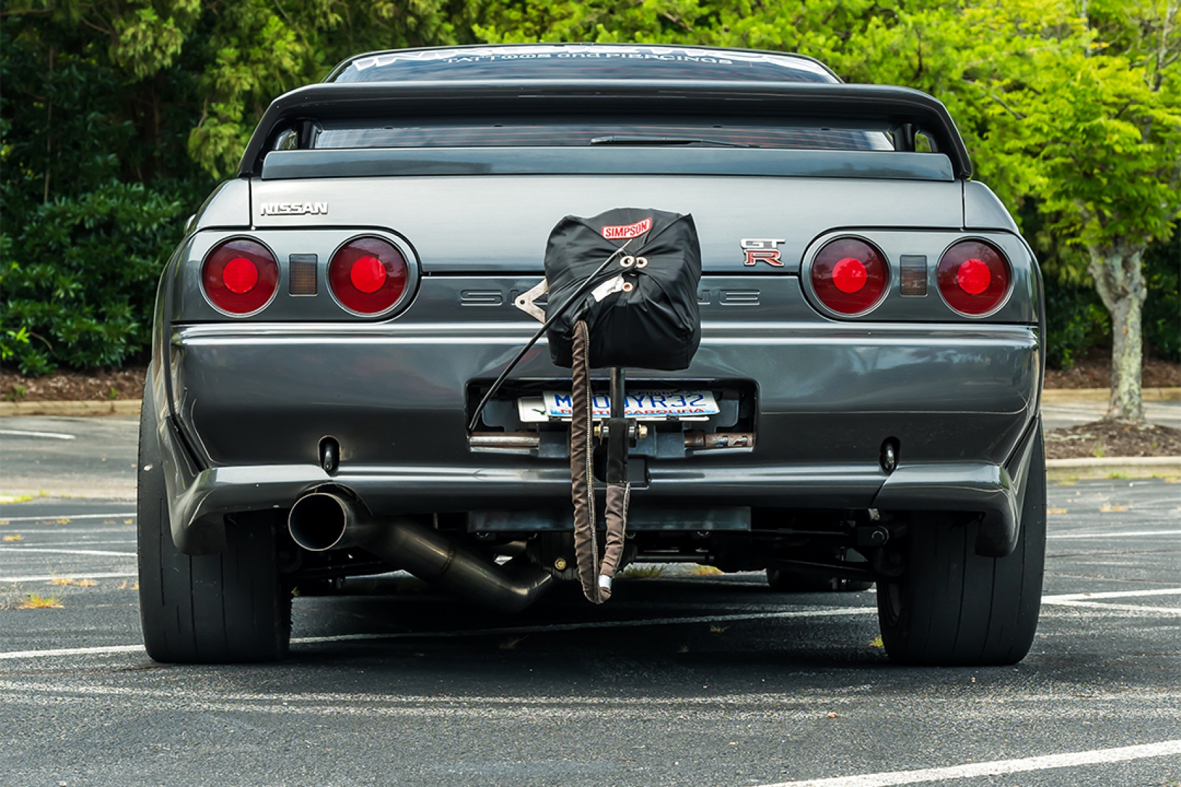 Rear view of Cee Vann’s gray 1990 Nissan Skyline GT-R showing the drag parachute, wide tires, large exhaust, and GT-R badging.