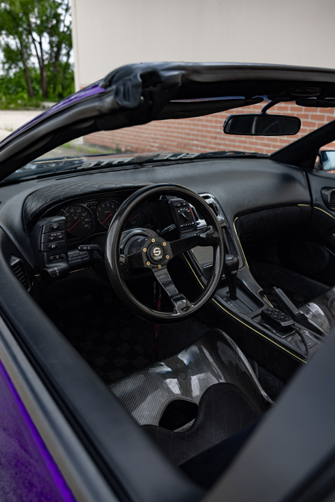 Interior detail of Alex Hammond’s 1993 Nissan 300ZX Convertible showing the carbon-fiber steering wheel, dashboard, center console, and custom interior trim.