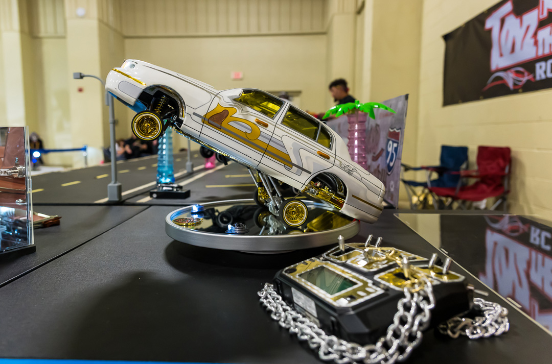 Custom RC lowrider car displayed in a hopping position with a detailed controller at Lowrider Super Show Charlotte 2026.