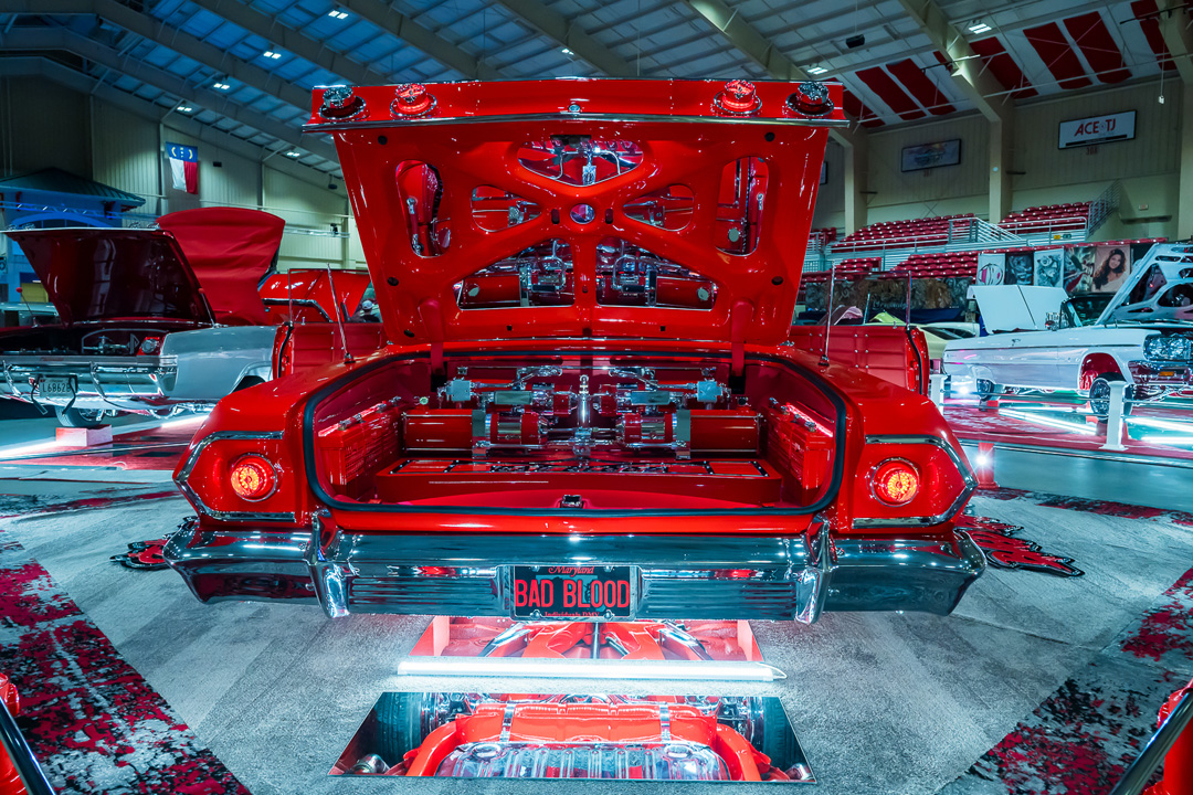 Red custom lowrider with detailed trunk display, chrome components, and underbody mirrors at Lowrider Super Show Charlotte 2026.