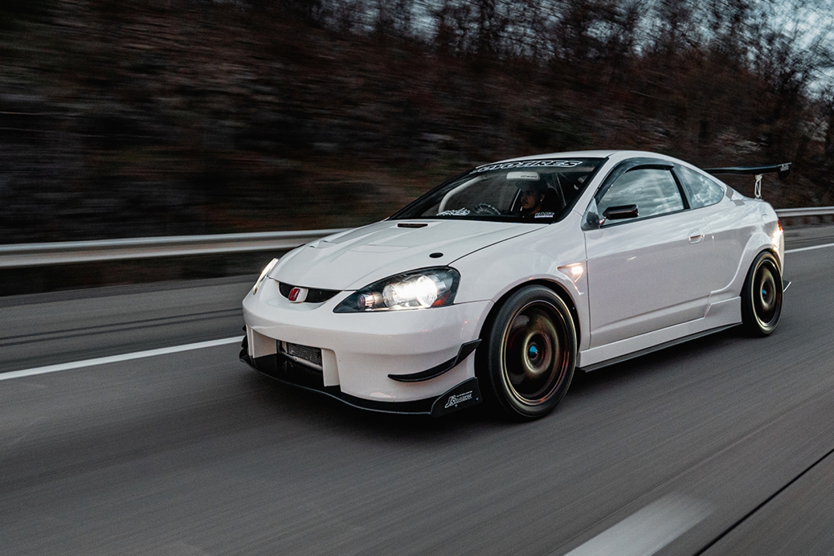 Moises Wynns’ Championship White 2003 Acura RSX rolling on the highway with J’s Racing aero, Mugen MF10 wheels, front splitter, and rear wing.