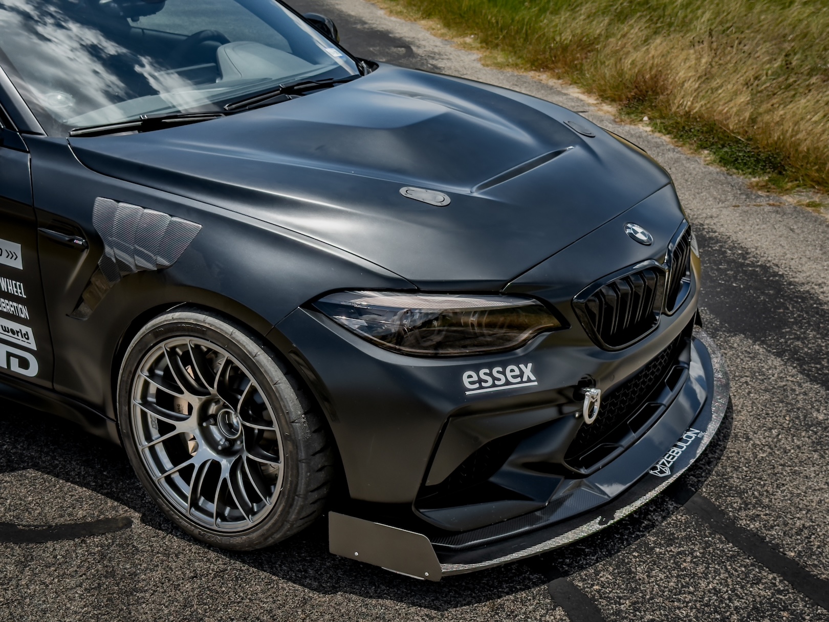 Front detail of Jason Merck’s black 2020 BMW M2 showing the hood, front splitter, wheel, and Essex decal.