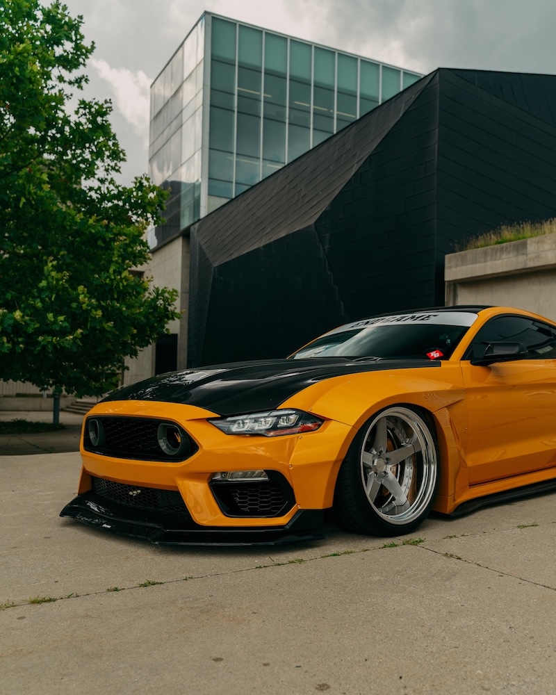 Front vertical view of Mussi Hussain’s Cyber Orange 2022 Ford Mustang GT showing the Robot Craftsman widebody aero, carbon hood, Mach 1 front-end conversion, Work Gnosis wheels, and low stance.