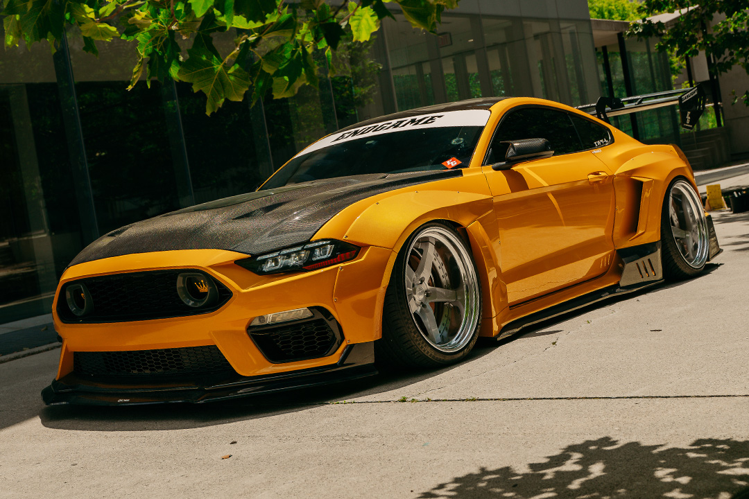 Mussi Hussain’s Cyber Orange 2022 Ford Mustang GT with Robot Craftsman widebody aero, Air Lift suspension, Work Gnosis wheels, custom lighting, carbon-fiber details, and reworked interior and trunk setup.