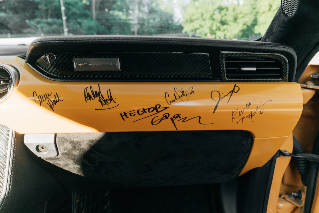 Mussi Hussain’s Cyber Orange 2022 Ford Mustang GT with Robot Craftsman widebody aero, Air Lift suspension, Work Gnosis wheels, custom lighting, carbon-fiber details, and reworked interior and trunk setup.