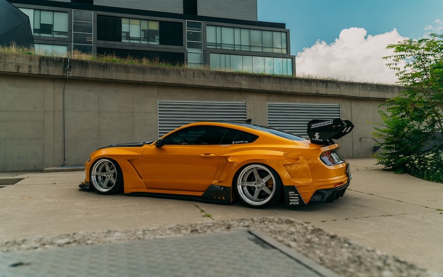 Mussi Hussain’s Cyber Orange 2022 Ford Mustang GT with Robot Craftsman widebody aero, Air Lift suspension, Work Gnosis wheels, custom lighting, carbon-fiber details, and reworked interior and trunk setup.