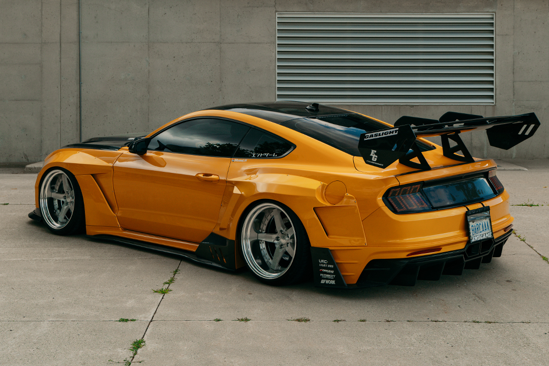 Rear three-quarter view of Mussi Hussain’s Cyber Orange 2022 Ford Mustang GT showing the Robot Craftsman widebody aero, large GT wing, rear diffuser, Work Gnosis wheels, and custom taillights.
