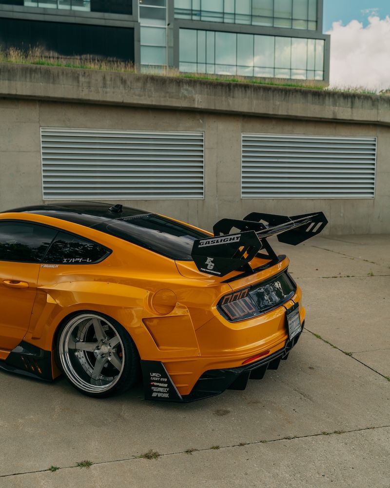 Rear vertical view of Mussi Hussain’s Cyber Orange 2022 Ford Mustang GT showing the Robot Craftsman widebody rear quarter, large GT wing, custom taillights, rear diffuser, and Work Gnosis wheel.