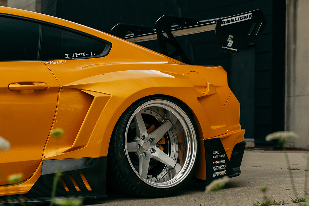 Rear quarter detail of Mussi Hussain’s 2022 Ford Mustang GT showing the polished Work Gnosis GR203 wheel, Robot Craftsman widebody rear over-fender, carbon side skirt extension, and GT sport wing.