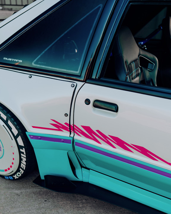 Regan McLaughlin’s 1988 Ford Mustang GT TimeFox with custom multi-tone paint, Ford Barra turbo swap, wide fiberglass fenders, retro Foxbody styling, HaloBLK wheel covers, custom interior, and nostalgic audio details.