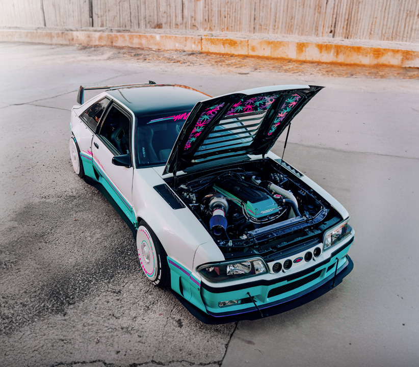 Regan McLaughlin’s 1988 Ford Mustang GT TimeFox with custom multi-tone paint, Ford Barra turbo swap, wide fiberglass fenders, retro Foxbody styling, HaloBLK wheel covers, custom interior, and nostalgic audio details.