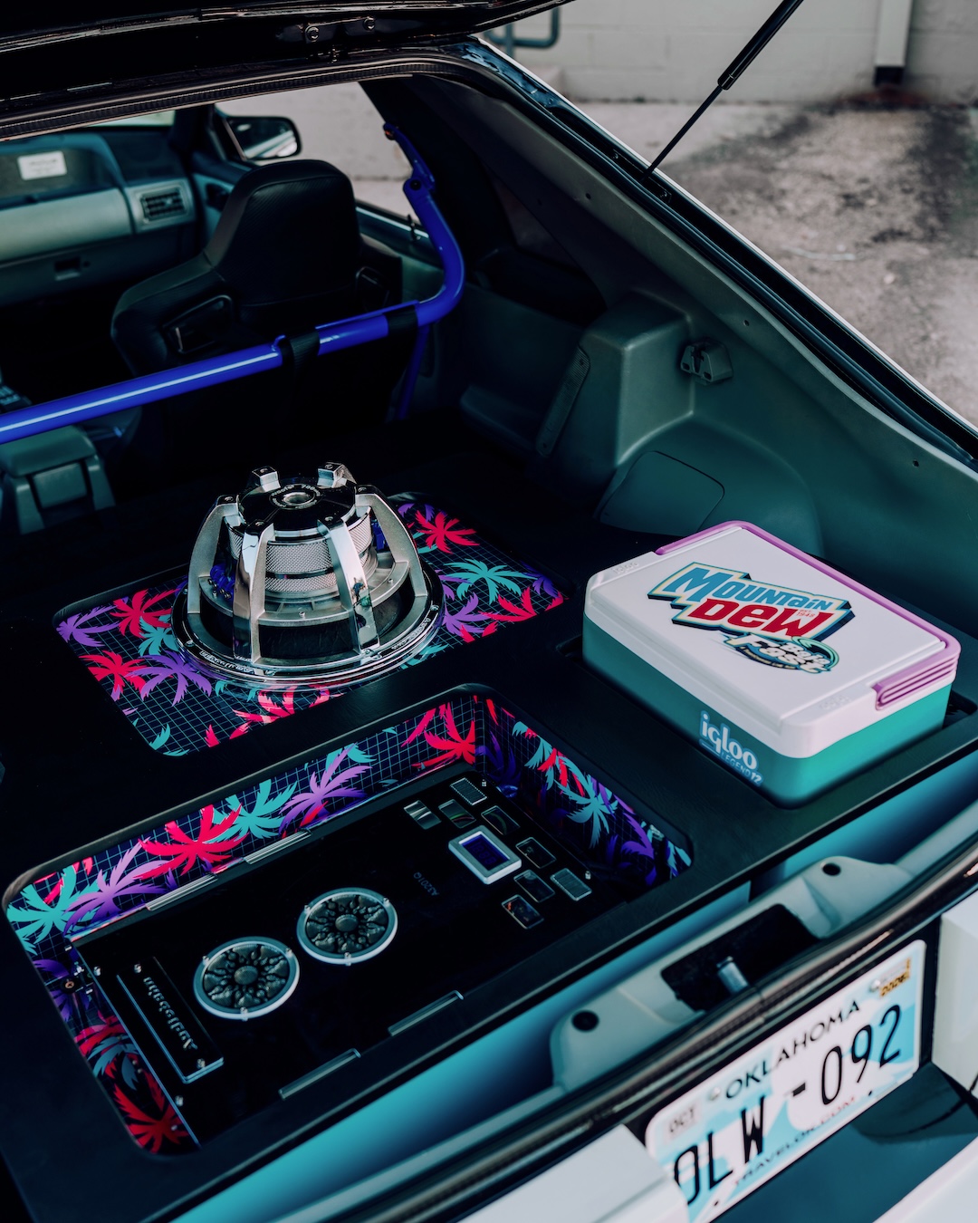 Hatch audio detail of Regan McLaughlin’s 1988 Ford Mustang GT TimeFox showing the custom subwoofer enclosure, Audiobahn audio setup, retro neon-style graphics, hatch delete, and Mountain Dew cooler.