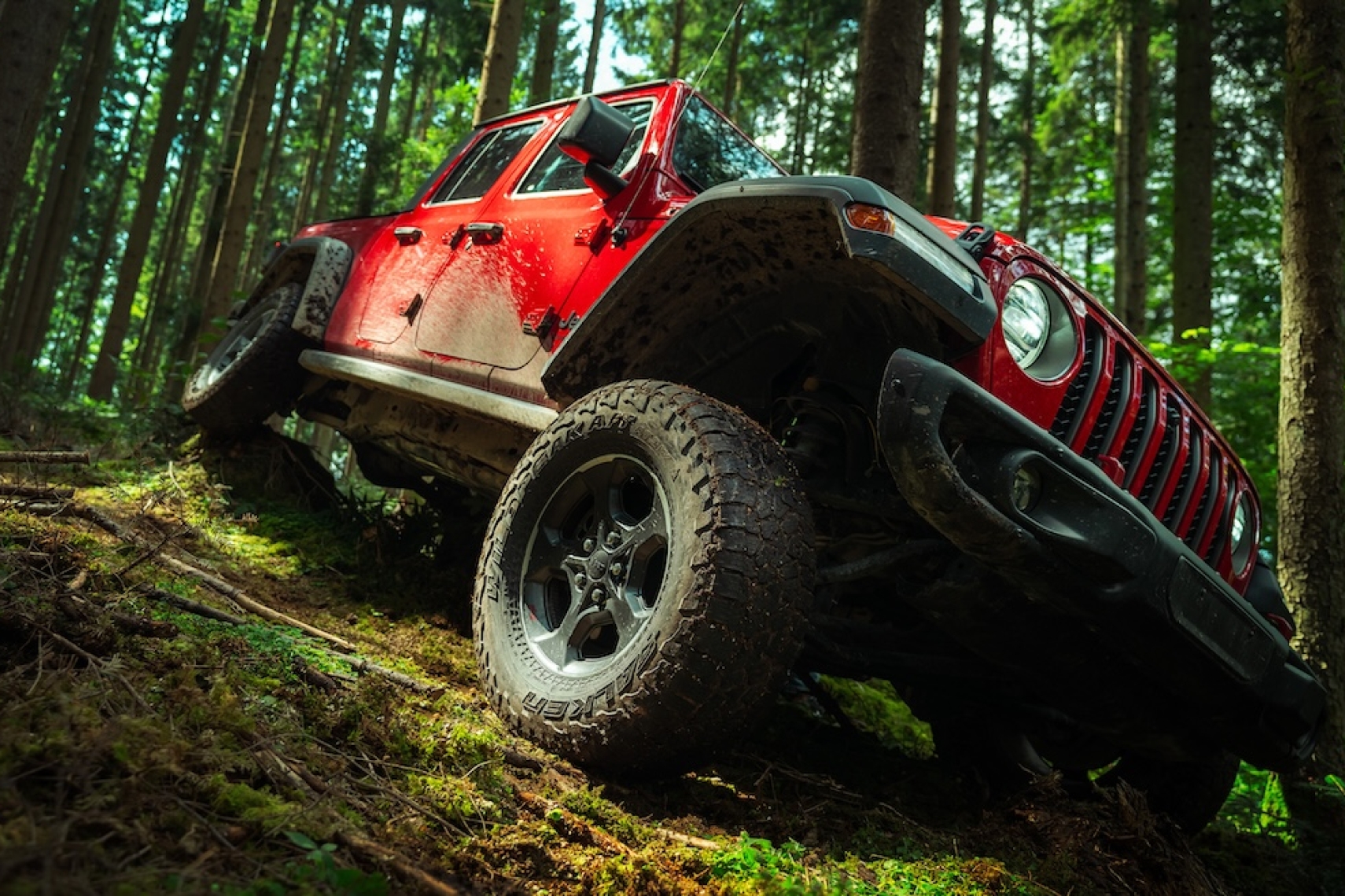 Red Jeep Gladiator driving off-road through a forest with Reiger Performance dampers installed.