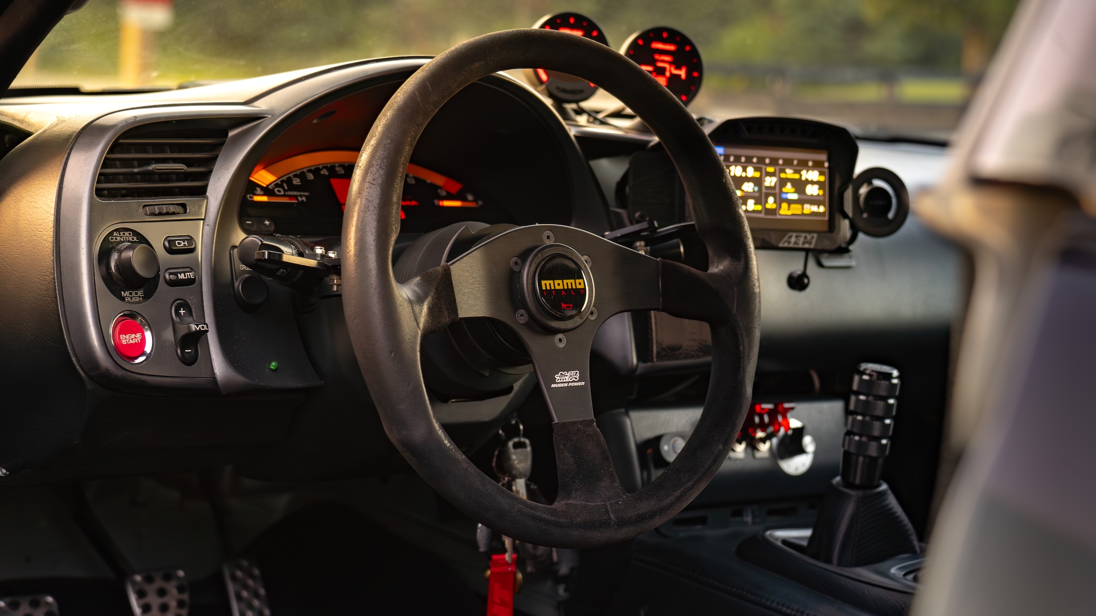 Cockpit detail of Thomas Wu’s 2002 Honda S2000 showing the steering wheel, AEM CD5 digital dash, Greddy Sirius gauges, shifter, and track-focused controls.