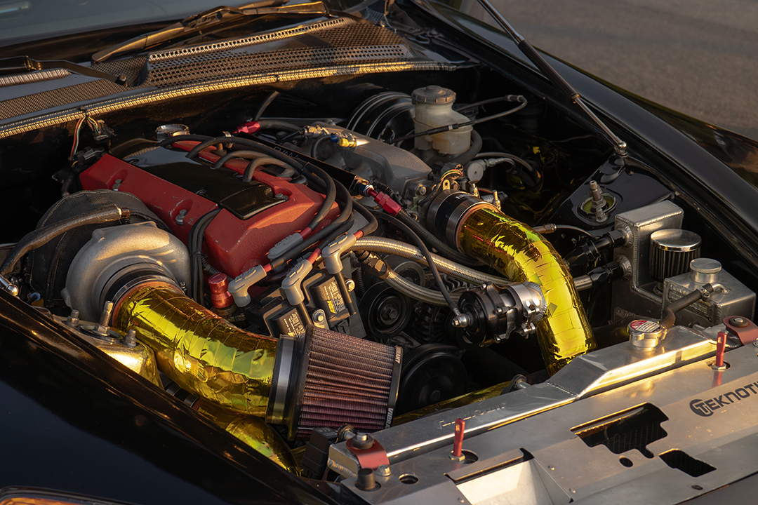 Engine bay detail of Thomas Wu’s 2002 Honda S2000 showing the turbocharged F20C setup, Precision 6466 turbo, tubular manifold, gold heat-wrapped charge piping, AEM smart coils, and custom performance hardware.