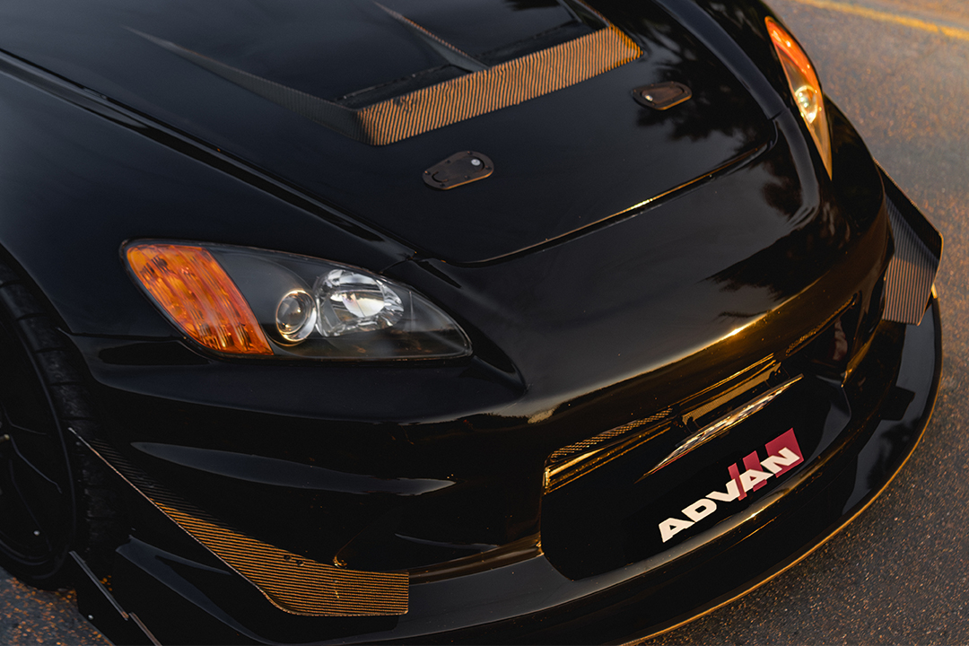 Front-end detail of Thomas Wu’s black 2002 Honda S2000 showing the Voltex-style front bumper, VIS Racing hood vent, headlight, front splitter, and track-focused aero.