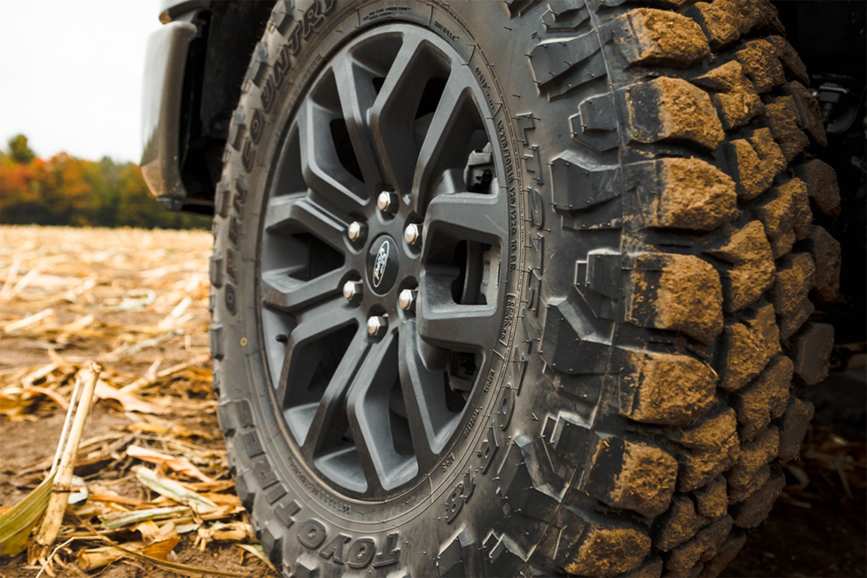 Close-up of a Toyo Open Country R/T Pro rugged terrain tire mounted on a Ford truck, highlighting its aggressive tread pattern and mud-covered shoulder blocks.